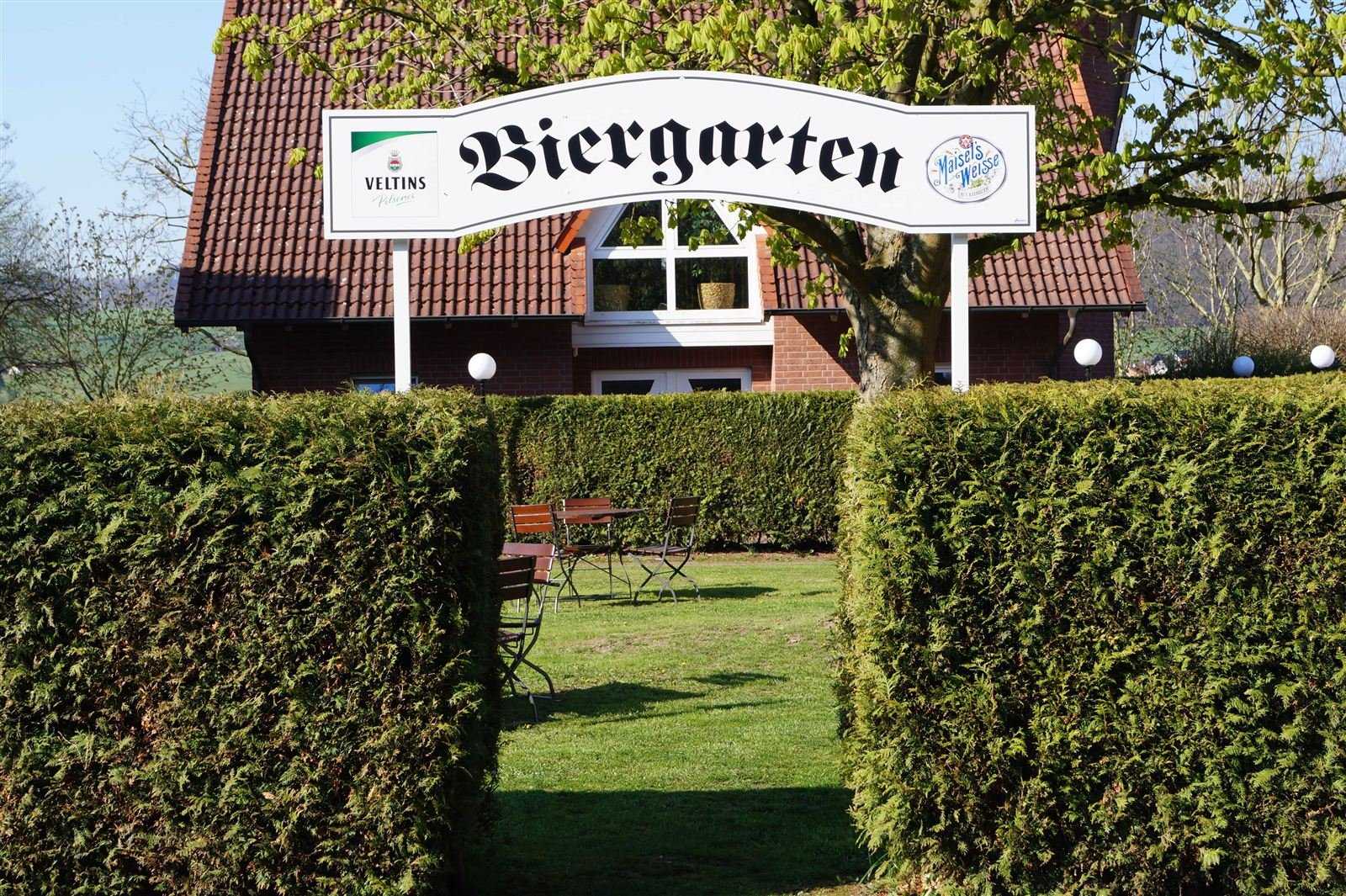 Eingang zum Biergarten mit Schild „Biergarten“ zwischen grünen Hecken